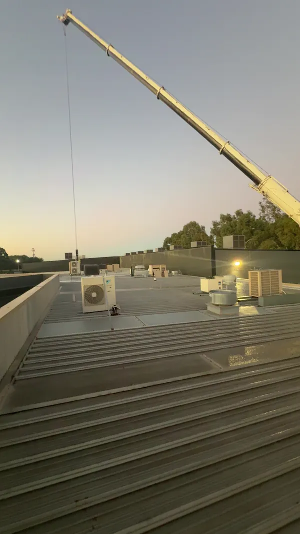Crane lifting HVAC equipment onto a commercial rooftop at dusk